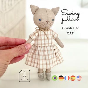 Può includere: Una bambola a forma di gatto fatta a mano con un vestito a quadri e stivali grigi. La bambola ha occhi blu e baffi. L'immagine include il testo "Sewing pattern" e "19CM/7,5" CAT".