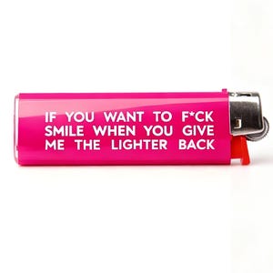 Pu&ograve; includere: Un accendino rosa acceso con il testo "IF YOU WANT TO F*CK SMILE WHEN YOU GIVE ME THE LIGHTER BACK" in bianco. L'accendino ha una parte superiore in metallo argentato e un interruttore di accensione rosso.