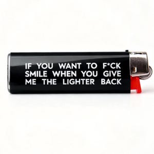 Pu&ograve; includere: Un accendino nero con la scritta "IF YOU WANT TO F*CK SMILE WHEN YOU GIVE ME THE LIGHTER BACK" in bianco. L'accendino ha una parte superiore in metallo argentato e una leva in plastica rossa.