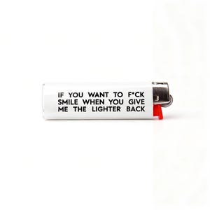 Puede incluir: Encendedor blanco con el texto "IF YOU WANT TO F*CK SMILE WHEN YOU GIVE ME THE LIGHTER BACK". El encendedor tiene un bot&oacute;n de encendido rojo y una parte superior de metal plateado.
