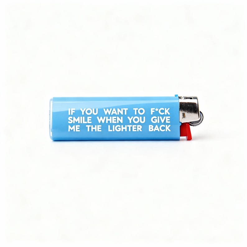 Pu&ograve; includere: Un accendino azzurro con la scritta "IF YOU WANT TO F*CK SMILE WHEN YOU GIVE ME THE LIGHTER BACK" in bianco. L'accendino ha un pulsante di accensione rosso e una parte superiore in metallo argentato.