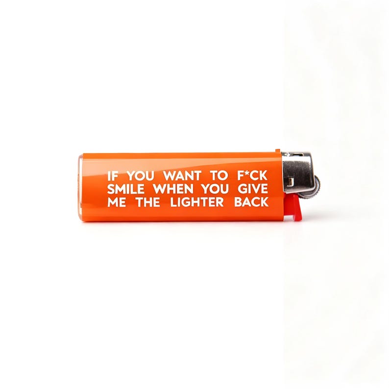Pu&ograve; includere: Accendino arancione con la scritta "IF YOU WANT TO F*CK SMILE WHEN YOU GIVE ME THE LIGHTER BACK." Presenta una parte superiore in metallo argentato e una leva in plastica rossa.