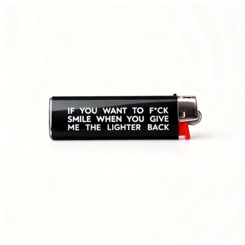 Puede incluir: Un encendedor negro con el texto "IF YOU WANT TO F*CK SMILE WHEN YOU GIVE ME THE LIGHTER BACK" en blanco. El encendedor tiene una parte superior de metal plateado y una palanca de pl&aacute;stico roja.