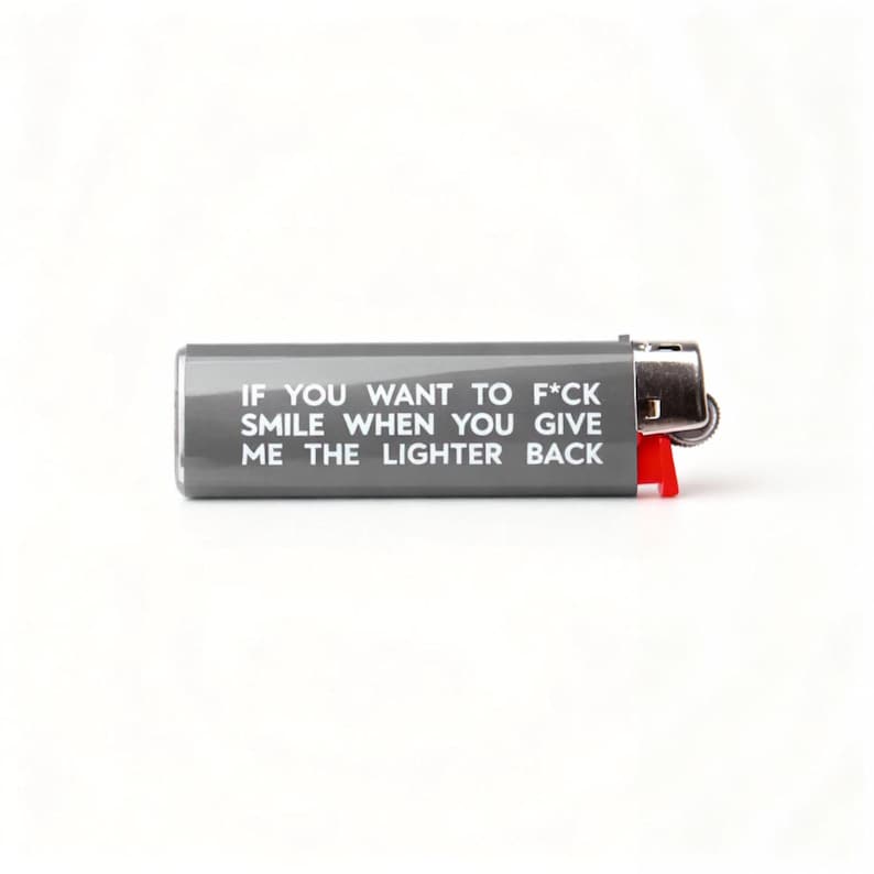 Puede incluir: Un encendedor gris con el texto "IF YOU WANT TO F*CK SMILE WHEN YOU GIVE ME THE LIGHTER BACK." El encendedor tiene un bot&oacute;n de encendido rojo y una parte superior de metal.