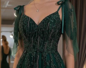 May include: Emerald green formal gown with a V-neckline and delicate spaghetti straps. The bodice is embellished with intricate beadwork and floral embroidery. Sheer, flowing sleeves are attached at the shoulders. A silver necklace with a pendant is visible.