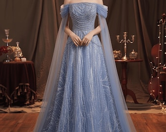 May include: A light blue off-the-shoulder gown with a beaded bodice and flowing skirt. The dress features delicate silver embellishments and sheer cape sleeves. The formal wear dress is suitable for special occasions.
