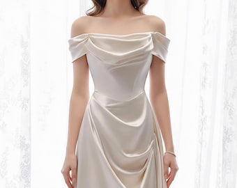 May include: An off-white, off-the-shoulder gown with a draped bodice and a flowing skirt. The dress has a satin finish and a subtle sheen. The design features a gathered detail at the waist and a soft, elegant silhouette, suitable for formal events.
