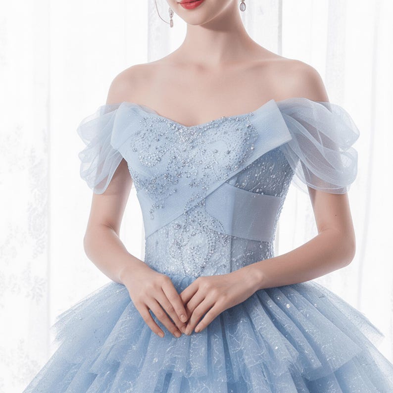 May include: A light blue off-the-shoulder gown with a layered skirt. The bodice features intricate beadwork and a crisscross design. The sleeves are made of sheer fabric, adding a touch of elegance to the formal dress.