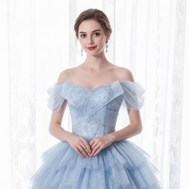 May include: A light blue off-the-shoulder gown with a layered tulle skirt. The bodice features intricate beadwork and a sweetheart neckline. The dress has sheer, puffed sleeves and is suitable for formal events.
