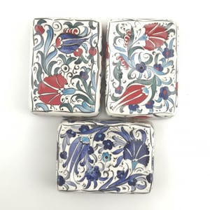 Könnte beinhalten: Drei rechteckige Keramik-Seifenschalen mit weißem Hintergrund und aufwendigen floralen Mustern in Blau, Rot und Grün. Die Muster zeigen stilisierte Blumen und Blätter.