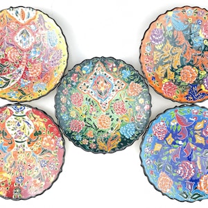 May include: Set of five colorful ceramic plates with intricate floral and geometric designs. The plates have a scalloped edge and a black rim.