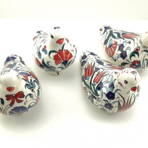 May include: Four ceramic bird figurines with white glaze and intricate floral patterns in red, blue, and green. The birds are all facing the same direction and have a slightly rounded shape.