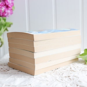 May include: A stack of six paperback books with cream-colored covers. The books are arranged vertically with the spines facing out. The top book has a blue cover with a light blue design.
