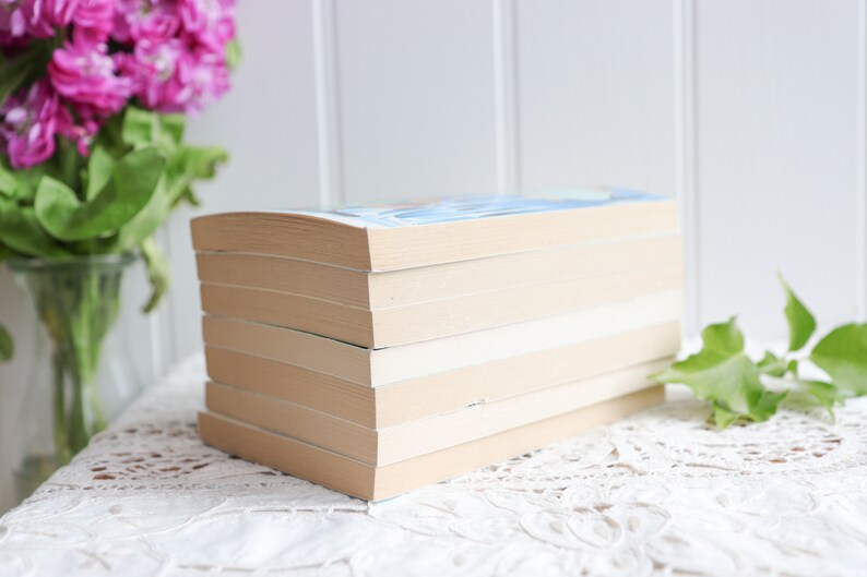May include: A stack of six paperback books with cream-colored covers. The books are arranged vertically with the spines facing out. The top book has a blue cover with a light blue design.