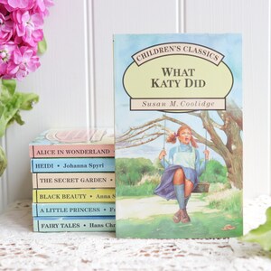 May include: A stack of classic children's books with titles like "Alice in Wonderland", "Heidi", "The Secret Garden", "Black Beauty", "A Little Princess", and "Fairy Tales".  The top book is "What Katy Did" by Susan M. Coolidge, featuring an illustration of a girl on a swing.