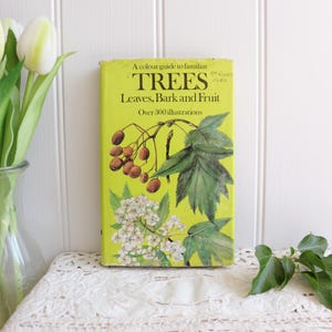 May include: A hardcover book titled A Colour Guide to Familiar Trees: Leaves, Bark and Fruit with a bright lime green cover featuring botanical illustrations of brown berries, green leaves, and white flowers, with over 300 illustrations noted.