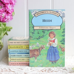 May include: A stack of vintage children's books with colorful covers. The top book is titled "Heidi" by Johanna Spyri. The book features a girl in a blue dress holding flowers and two goats in a green field.