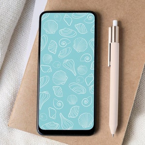 May include: A smartphone displays a teal seashell pattern. A beige pen rests on a brown notebook, next to a white cup of coffee on a cork coaster. A white fabric is in the background.