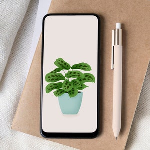 May include: A smartphone displays a digital illustration of a potted plant with green leaves and a light blue pot. A beige pen and a cup of coffee sit nearby on a brown surface, next to a white cloth.