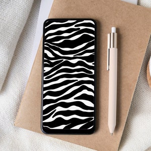 May include: A smartphone with a black and white zebra print screen sits on a brown paper notebook. A beige pen and a white cup of coffee are also on the surface. The cup sits on a small cork coaster.