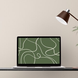 May include: A laptop displays a green abstract design with white swirling lines. The laptop is open on a black desk, with a brown desk lamp and a plant in the background. The screen's design is minimalist.