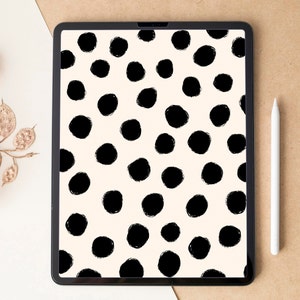 Puede incluir: Una tableta digital muestra un patrón de grandes círculos negros con pinceladas sobre un fondo crema. Un lápiz óptico blanco descansa junto a la tableta. A la izquierda, vainas de semillas secas y doradas.