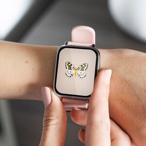 Może przedstawiać: Kwadratowy smartwatch z jasnor&oacute;żowym paskiem i srebrną kopertą. Tarcza zegarka przedstawia motyw motyla z czarnymi i ż&oacute;łtymi kropkami. Zegarek jest trzymany przez osobę.