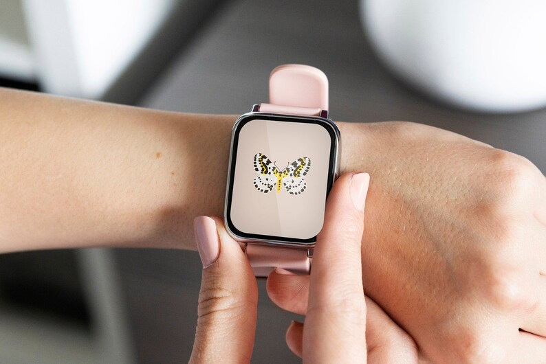Może przedstawiać: Kwadratowy smartwatch z jasnor&oacute;żowym paskiem i srebrną kopertą. Tarcza zegarka przedstawia motyw motyla z czarnymi i ż&oacute;łtymi kropkami. Zegarek jest trzymany przez osobę.