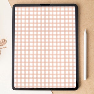 Puede incluir: Una tableta digital con una pantalla que muestra un patrón de cuadros de color melocotón y blanco. Un lápiz óptico blanco descansa junto a la tableta sobre una superficie marrón. Hay vainas de semillas secas en la esquina superior izquierda.