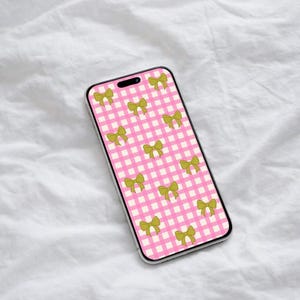 Puede incluir: Un smartphone con un patrón de cuadros rosas y lazos verde oliva. La funda del teléfono tiene un marco plateado y se muestra sobre una superficie blanca texturizada.