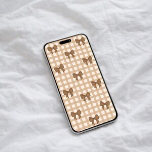 Puede incluir: Una funda de teléfono inteligente con un patrón repetido de lazos marrones sobre un fondo a cuadros beige y blanco. La funda tiene un borde transparente y se muestra sobre una superficie blanca texturizada.