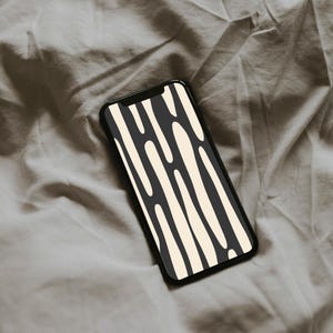May include: A black smartphone showing a cream and black abstract design of vertical, irregular shapes. The phone is placed on a wrinkled, grey fabric surface.