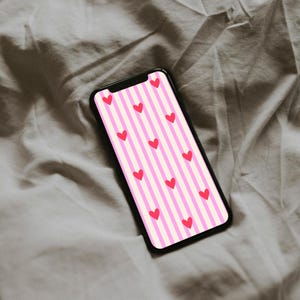 May include: A black smartphone shows a pink and white striped pattern with red hearts. The phone rests on a grey, creased fabric, creating a simple, yet visually appealing composition.