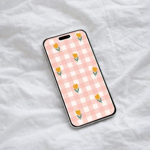 Puede incluir: Un teléfono inteligente con un fondo de patrón de cuadros rosa y gráficos de flores de tulipanes amarillos. El teléfono se muestra sobre una superficie blanca y texturizada.