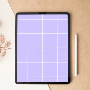 Puede incluir: Una tableta negra con una pantalla de cuadrícula lavanda y un lápiz óptico blanco. Una rama decorativa con hojas doradas está a la izquierda. La tableta está sobre una superficie beige y blanca.