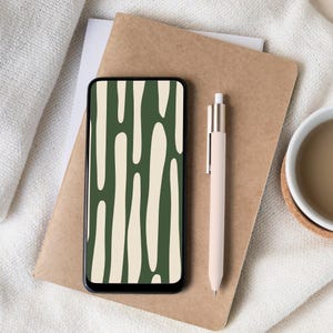 May include: A smartphone displaying a green and cream abstract design sits on a brown notebook. A pale pink pen and a white mug with a brown liquid are also present. The items are arranged on a white, textured surface.