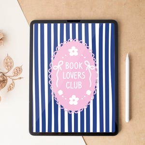 May include: A black tablet displays a pink oval with the text "BOOK LOVERS CLUB" against a blue and white striped background. A white stylus rests beside the tablet on a tan surface.