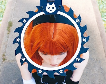 May include: A person wearing a black and white outfit with a large black circular saw blade accessory on their head. The saw blade has a white cat head with an 'X' on it. The person has long red hair.