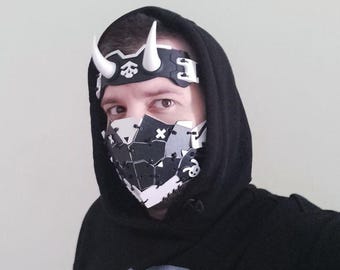 May include: A black hoodie with a graphic print and a matching mask and headband. The mask and headband are black and white with geometric shapes and skull details. The headband has white horns.