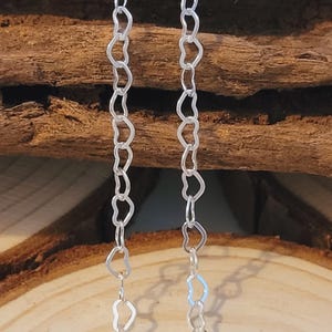 May include: A silver chain necklace with heart-shaped links. The chain is displayed on a wooden surface.