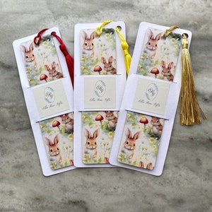 May include: Three bookmarks featuring a bunny rabbit pattern and a tassel. The bookmarks are white with a white border and the text "Ella Rose Gifts" in a circle. The tassels are red, yellow, and gold.