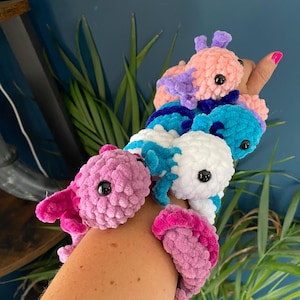 May include: A collection of colorful, plush axolotl toys in shades of pink, blue, purple, and white. Each axolotl has black button eyes and a frilly, contrasting gill design. The toys are soft and cuddly, perfect for children.