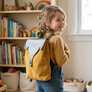 Könnte beinhalten: Ein senfgelber und olivgrüner Rucksack mit einem Elefantenmuster auf der Klappe. Der Rucksack ist aus Wildleder und Leder gefertigt, mit verstellbaren Trägern und einem Knopfverschluss. Perfekt für Schule oder Reisen.