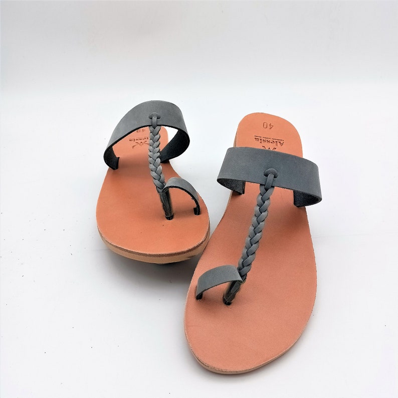 May include: A pair of gray leather sandals with braided straps and toe loops. The sandals have a light brown sole and a gray strap across the top of the foot. The sandals are size 40.