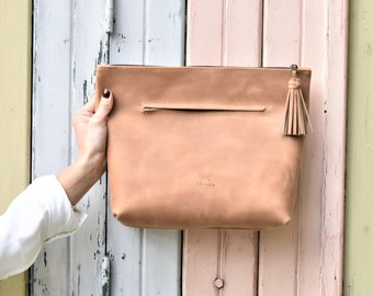 May include: A light brown leather clutch with a tassel zipper pull. The clutch has a small back pocket and the brand name "Alessia" is embossed on the front. The background is a colorful wooden door.