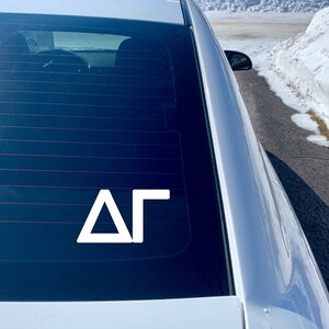 May include: A white vinyl decal with the letters "&Delta;&Gamma;" on a black car window.