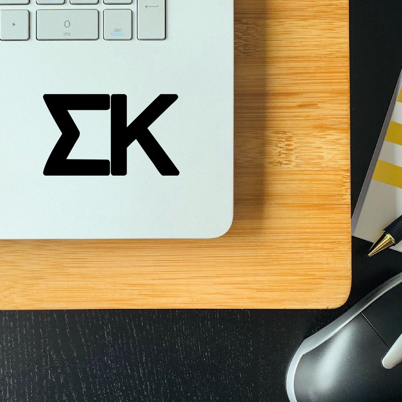 May include: A white laptop with a black "&Sigma;&Kappa;" sticker on the top. The laptop is sitting on a wooden surface. A black computer mouse is in the lower right corner of the image.