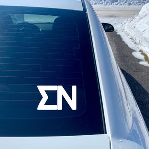 May include: A white vinyl decal with the letters "&Sigma;N" on a black car window.