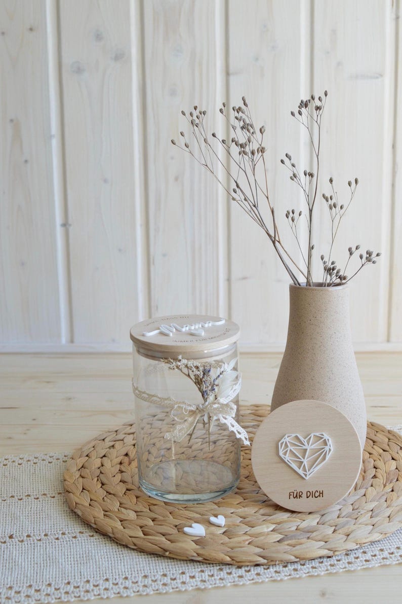 May include: A glass jar with a wooden lid and a small bouquet of dried flowers inside. The jar is sitting on a woven placemat with a wooden heart-shaped sign that says "F&uuml;r Dich" in German.