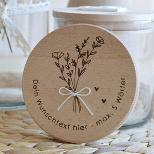 May include: A wooden round jar lid with a floral design and the text "Dein Wunschtext hier - max. 5 W&ouml;rter" engraved on it.